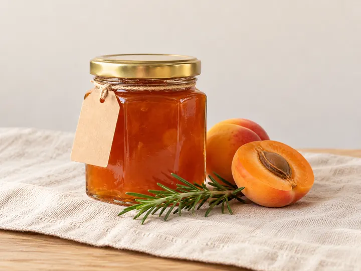 Pot de confiture d'abricot, abricots frais coupés et brin de romarin