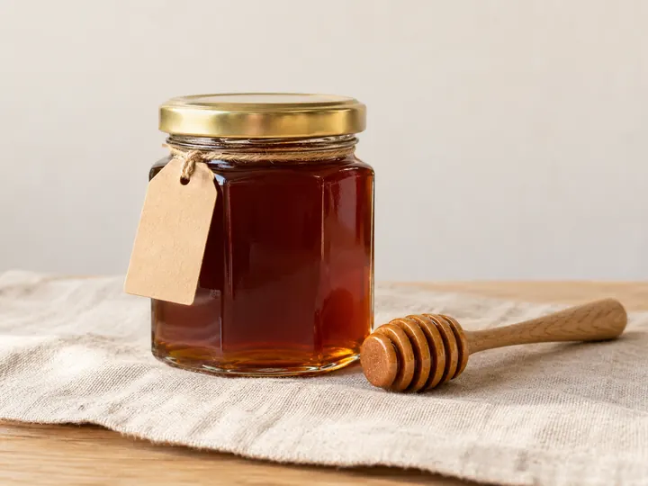 Pot de miel de châtaignier ambré et sa cuillère en bois, posés sur une toile de lin